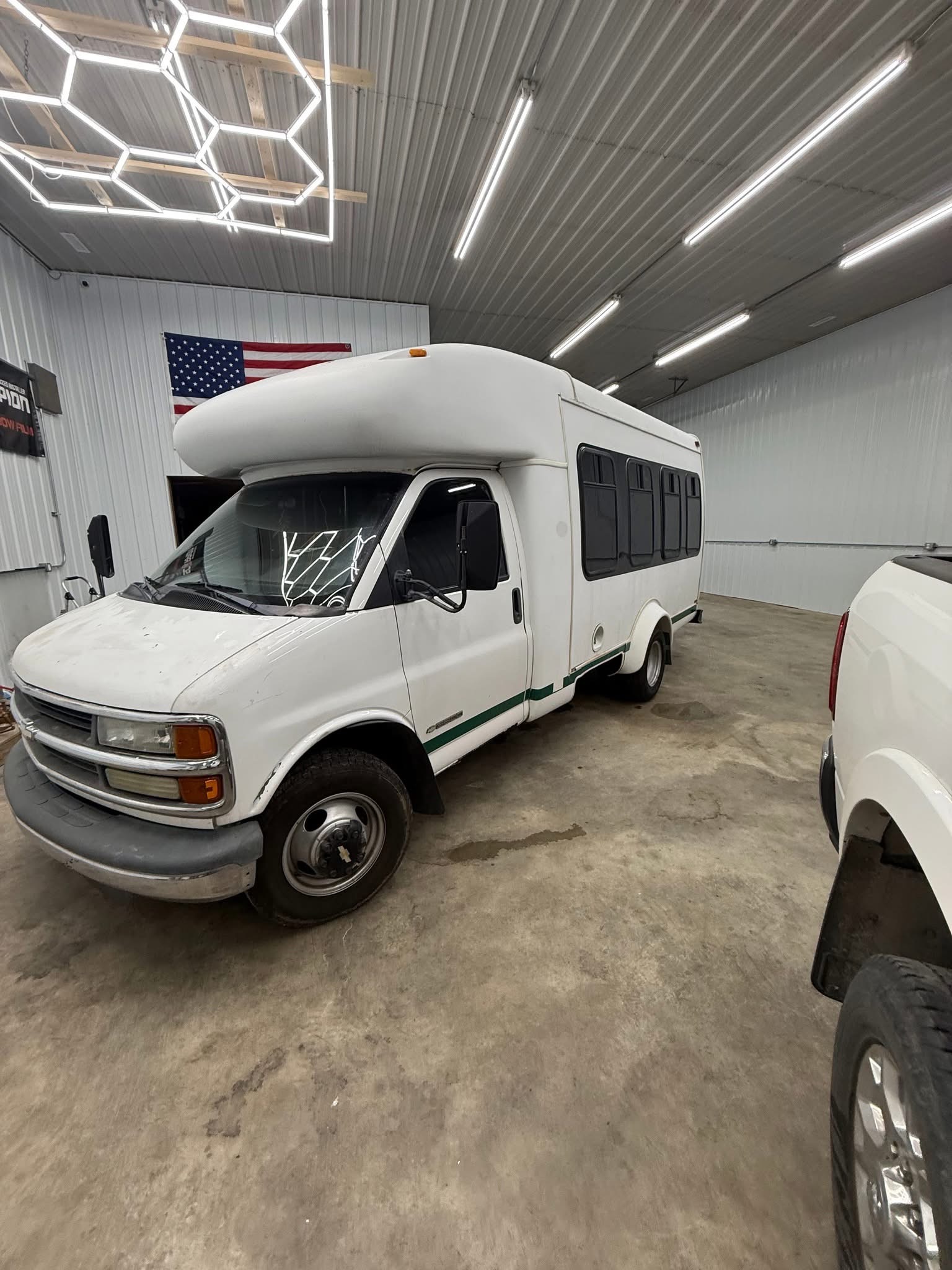 Three-quarter front exterior view of the white 14-passenger party bus parked indoors